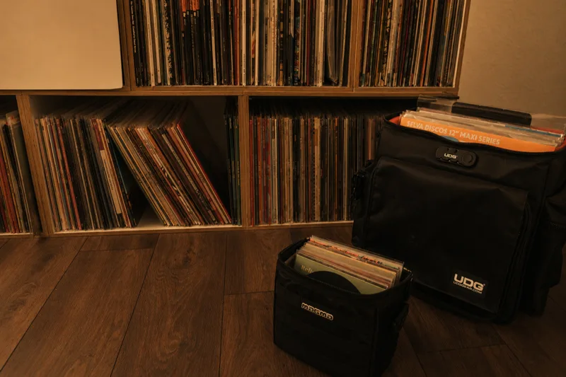 A DJ pulling vinyl records from a shelf into a record bag under warm club lighting