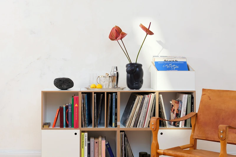 A low, wide stocubo sideboard with eight compartments of records and books next to a leather armchair